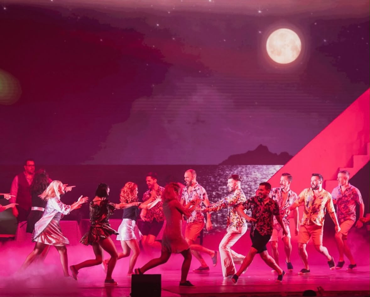 Dancers performing in Mamma Mia at Sala Palatului beneath pink stage lighting